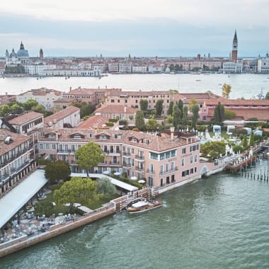 Aerial view of the Belmond Hotel Cipriani along a canal with the cityscape of Venice in the background.