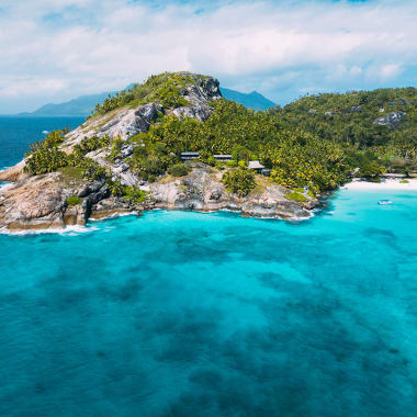 Eine tropische Insel mit üppigem Grün, felsigen Klippen und einem weißen Sandstrand, umgeben von türkisfarbenem Wasser.