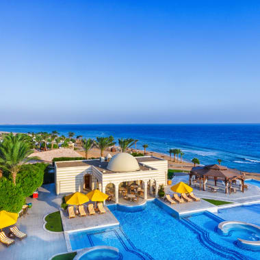 Ein luxuriöses Resort mit mehreren Pools und gelben Sonnenschirmen mit Blick auf den Ozean in Ägypten.