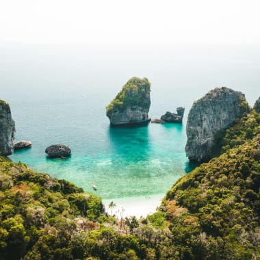 Ein abgelegener Strand, umgeben von steilen, grünen Klippen und smaragdgrünem Wasser in Thailand