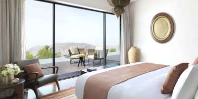 Ein Schlafzimmer mit einer großen glasschiebewand, die zu einem Balkon mit Sitzgelegenheiten und Blick auf die Berge führt.