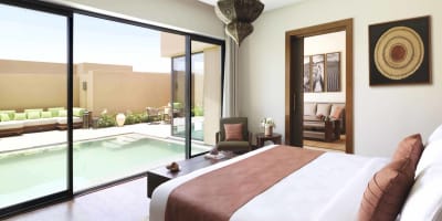 Ein luxuriöses Schlafzimmer mit einem großen Bett, braunen Akzenten und Blick auf einen privaten Pool außerhalb durch Schiebetüren.