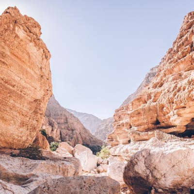 Ein tiefer felsiger Canyon mit großen Steinen und steilen Klippen unter klarem Himmel in Wadi Shab, Oman.