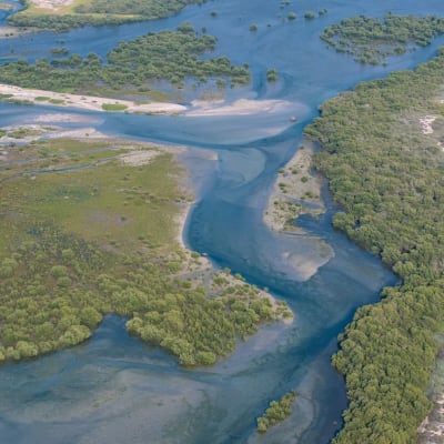 Aerial view of a lush river winding through green landscapes and sandy areas near a resort.