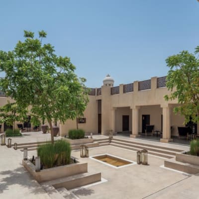 Courtyard with trees, planters, and steps leading to the building entrances at The Chedi Al Bait in Sharjah.
