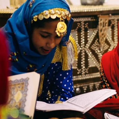 Omanisches Mädchen in traditioneller Kleidung, lernend mit Büchern in einer dekorierten Umgebung.