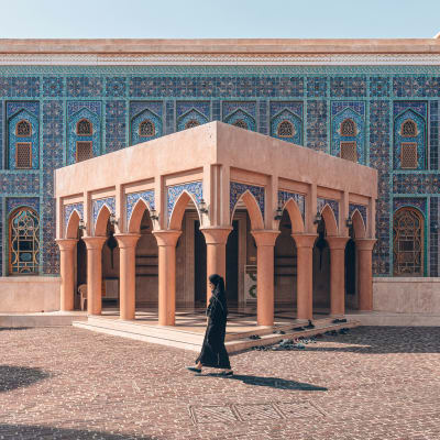 Eine Frau läuft vor einem Gebäude mit pinkfarbenen Bögen und blauen Fliesenwänden in Doha.