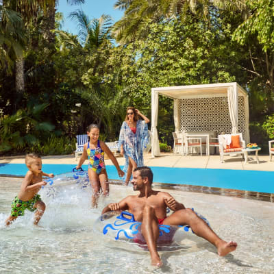 A family enjoying a day at a water park with lush greenery in the background and cabanas nearby.