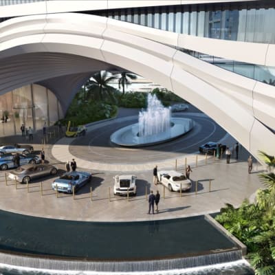Luxury hotel entrance with several parked cars, a fountain, and lush greenery.