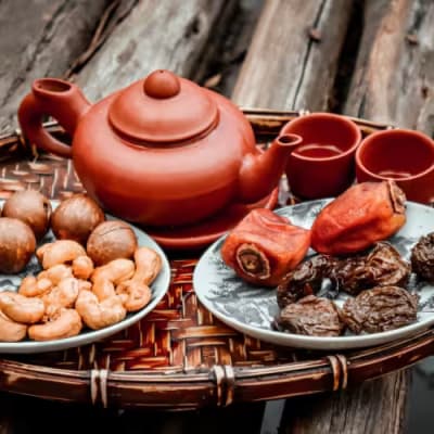 Traditional Saudi Arabian food served on a woven tray, including dates, nuts, a teapot, and cups.