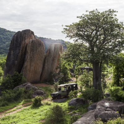 Safari Fahrzeug faehrt durch gruene und felsige Landschaften