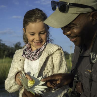 Ein junges Mädchen lächelt, während ein erfahrener Safari-Guide ihr eine weiße Blume zeigt.