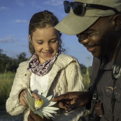 A young girl and a guide observe a bird with a female flower in a natural outdoor setting.