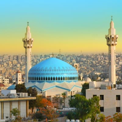 Die bläulich gekrönte Moschee mit zwei Minaretten ragt prominent in der Stadtlandschaft von Amman bei Sonnenuntergang.