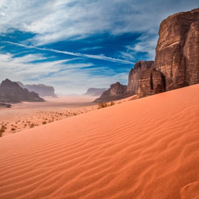 Weites Wüstenland mit roten Sanddünen, hohen Felsformationen und einem teilweise bewölkten Himmel im Jordanien Wadi Rum.