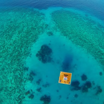 An aerial view of a water bungalow on clear turquoise ocean waters, surrounded by coral reefs near Pemba Island.