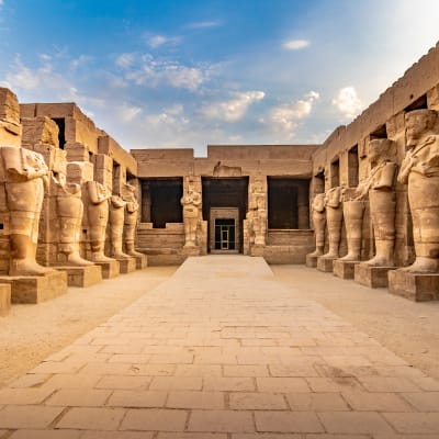 Luxor-Tempel in Ägypten, zeigt Reihen alter Statuen entlang des Weges, der zur Eingangstür führt, unter einem partly cloudy Himmel.