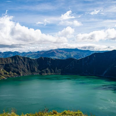Ein Kratersee mit steilen, grünen Kraterwänden unter einem partly Cloudy-Himmel.