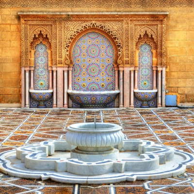Ein verzierter Brunnen mit einer gemusterten Wand und aufwändigem Design im Hintergrund, auf einem verzierten Hof.