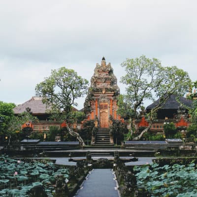 A traditional Balinese temple surrounded by lush greenery and a pond with lotus flowers in Ubud, Bali, Indonesia.