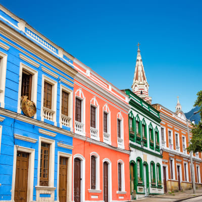 Colorful colonial-style houses in a vibrant neighborhood of Bogotá, Colombia with a church steeple in the background.