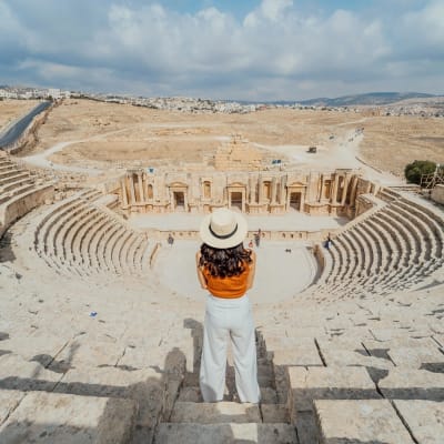 Eine Frau steht im antiken römischen Amphitheater in Jordanien, mit Blick auf die Bühne und die umliegende Wüstenlandschaft.