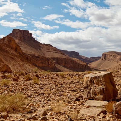 Eine rauhe Wüstenlandschaft in den Atlasbergen in Marokko, mit großen Steinen und bergigem Gelände unter einem teils bewölkten Himmel.