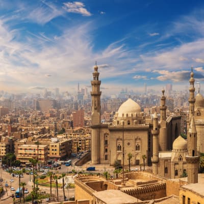 Panoramablick auf Kairo mit Sultan Hassan Moschee und Stadtbild unter einem teilweise bewölkten Himmel.