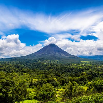 A lush green landscape with the Arenal Volcano erupting under a partly cloudy sky in Costa Rica.