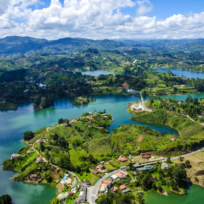 A scenic aerial view of lush green lakes and rolling hills in Colombia with scattered houses and a winding road.