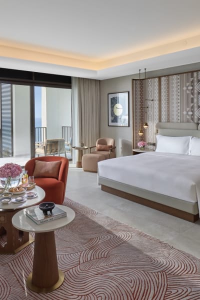 Ein luxuriöses Schlafzimmer mit einem neutralfarbenen Bett, dekorativen Pendelleuchten und einer gemusterten Akzentwand im Hintergrund.