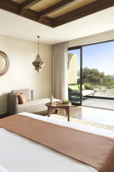 Ein geräumiges Hotelzimmer mit Balkonblick auf die Natur und Berge in Oman.