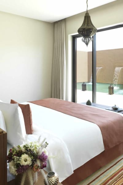 Das Hauptschlafzimmer verfügt über ein großes Bett mit weißen Bettwäsche und einem pinkfarbenen Bettläufer, mit Schiebetüren, die zu einer privaten Terrasse mit Sitzgelegenheiten und einem Pool führen.