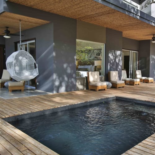 Moderner Außenpoolbereich mit Holzdeck, Liegestühlen und einer Hängesessel neben einem modernen Gebäude.