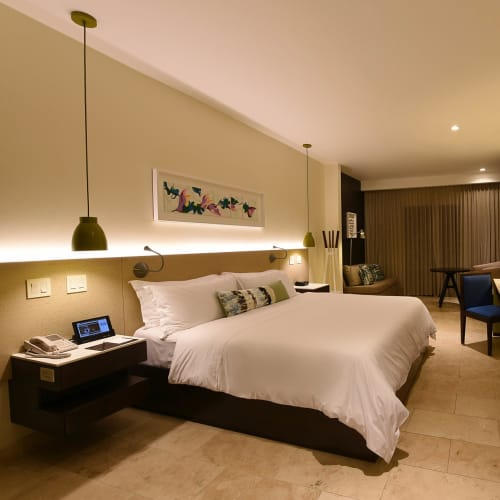 Ein Hotelzimmer mit großem Bett, an der Wand montiertem Fernseher und einem Arbeitsplatz in der Nähe eines Fensters mit Vorhängen.
