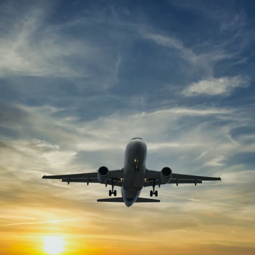 A commercial airplane is flying low against a sunset sky with scattered clouds.
