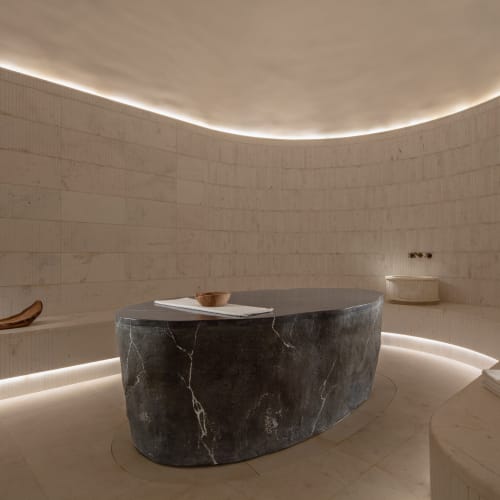 Ein modernes Spa-Zimmer mit gewölbten weißen Wänden, sanfter Beleuchtung und einem schwarzen Marmor-Tisch in der Mitte.