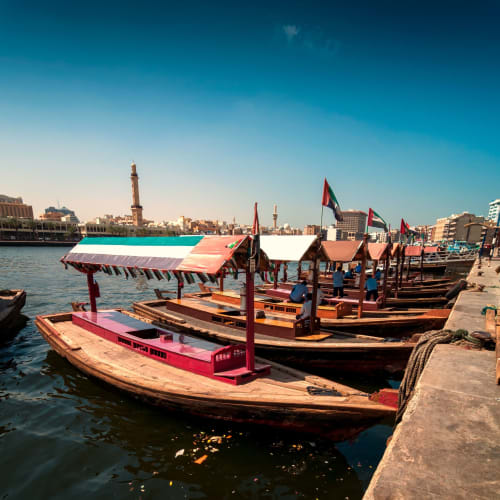 Traditionelle Abra-Schiffe am Dock entlang des Deira Creek in Dubai mit Stadtgebäuden im Hintergrund.