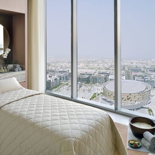 Ein gemütliches Schlafzimmer mit einem Einzelbett, großem Fenster mit Blick auf die Stadt und einem Spiegel mit Blumen an der Seite.