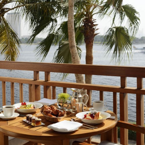 Ein Frühstück auf einem Holzbalkon mit Blick auf den Fluss, Palmen und ein Boot im Wasser.