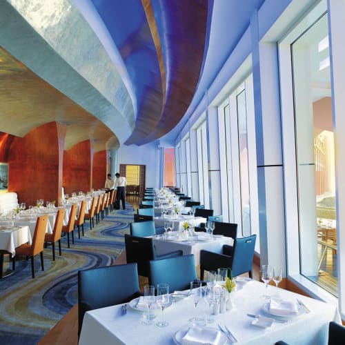 Elegantes Restaurant-Innere mit weißen Tafeldecken und großen Fenstern mit Blick auf einen Außenbereich.