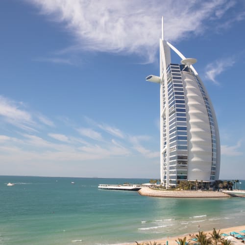 The Burj Al Arab hotel, a luxury hotel with a sail-shaped structure, situated on the coast of Dubai under a partly cloudy sky.