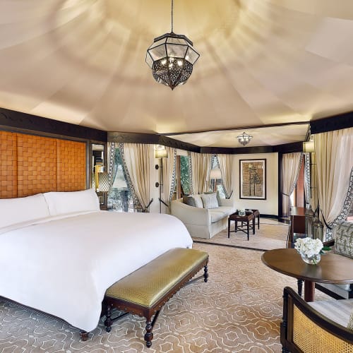 Luxuriöses Schlafzimmer mit großem weißen Bett, dekorativen Vorhängen und eleganten Möbeln in einer geräumigen Hotel-Suite.