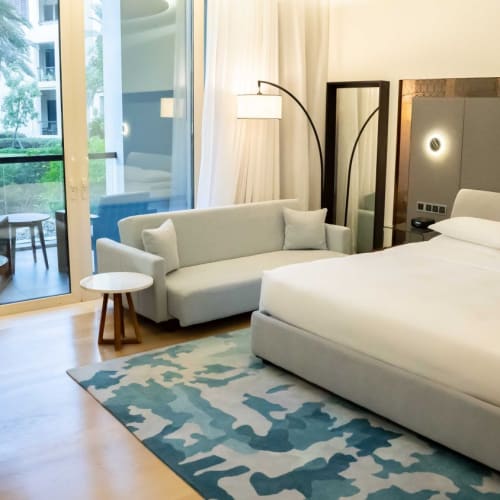 Ein modernes Hotelzimmer mit einem großen Bett, einem Sofa, einem kleinen Tisch und Balkon mit Außensitzgelegenheiten, Blick auf eine grüne Umgebung.