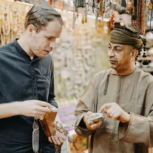 Ein junger Mann mit heller Haut und ein Mann im Nahen Osten mit dunkler Haut kaufen in einem farbenfrohen Souvenirmarkt ein.