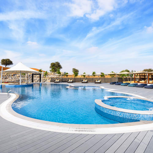 Ein luxuriöser Außenpool mit Hot Tub, in einem sonnigen Wüstenresort mit Palmen und Liegeflächen.