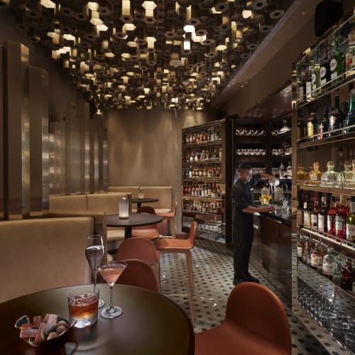 Elegante Bar-Inneneinrichtung mit einem Barkeeper, der Getränke serviert, umgeben von Regalen mit Spirituosen und moderner Dekoration.