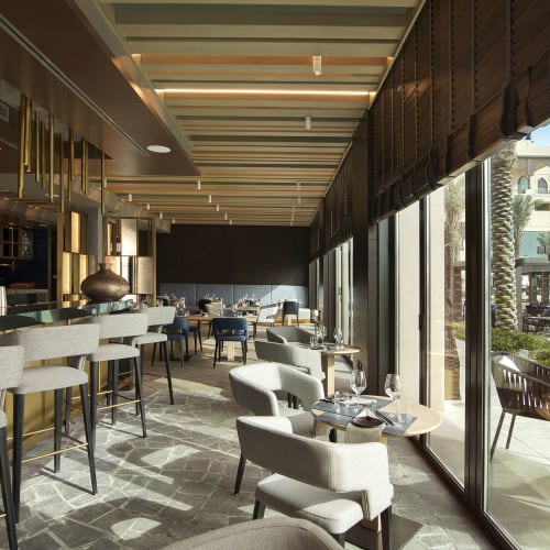 Luxurious and modern restaurant interior with high ceiling, bar area, and large glass windows offering a view outside.