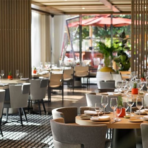 Elegantes Restaurantinterieur mit runden Tischen, die zum Essen vorbereitet sind, große Fenster und natürliches Licht.