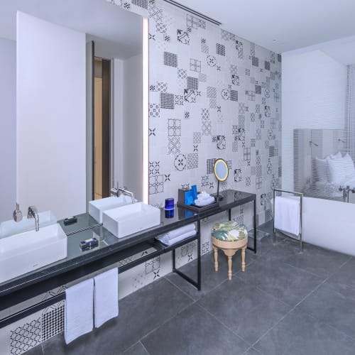 Ein modernes Badezimmer mit Doppelwaschbecken, dekorativen Wandfliesen und einem separaten Bereich mit Badewanne und Fenster.